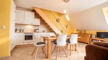 Eine moderne Küche mit weißen Schränken, einer Holztreppe und einem Essbereich inklusive Tisch und Stühlen.