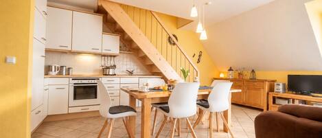A modern kitchen with white cabinets, a wooden staircase, and a dining area with a table and chairs.