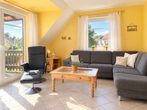 Sala de estar con sofá, sillón y mesa de centro, un balcón con vistas y una pared amarilla.