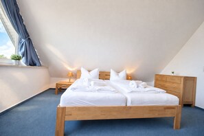 Un dormitorio con cama de madera, dos mesitas de noche, un tocador y un armario, junto a una ventana con cortinas.