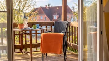 Eine Holzdar Terrasse mit einem Stuhl, einem Tisch, einer Topfpflanze und Blick auf Häuser im Hintergrund.