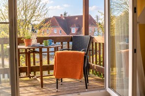 Eine Holzdar Terrasse mit einem Stuhl, einem Tisch, einer Topfpflanze und Blick auf Häuser im Hintergrund.