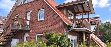 A two-story house with a sloped roof, a wooden balcony, and a visible staircase leading to the upper floor.
