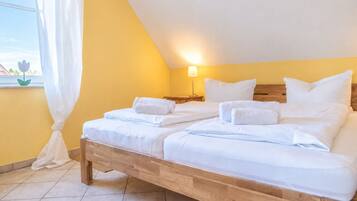Ein Doppelbett mit weißen Laken, ein Nachttisch mit Lampe und ein Fenster mit Vorhängen.