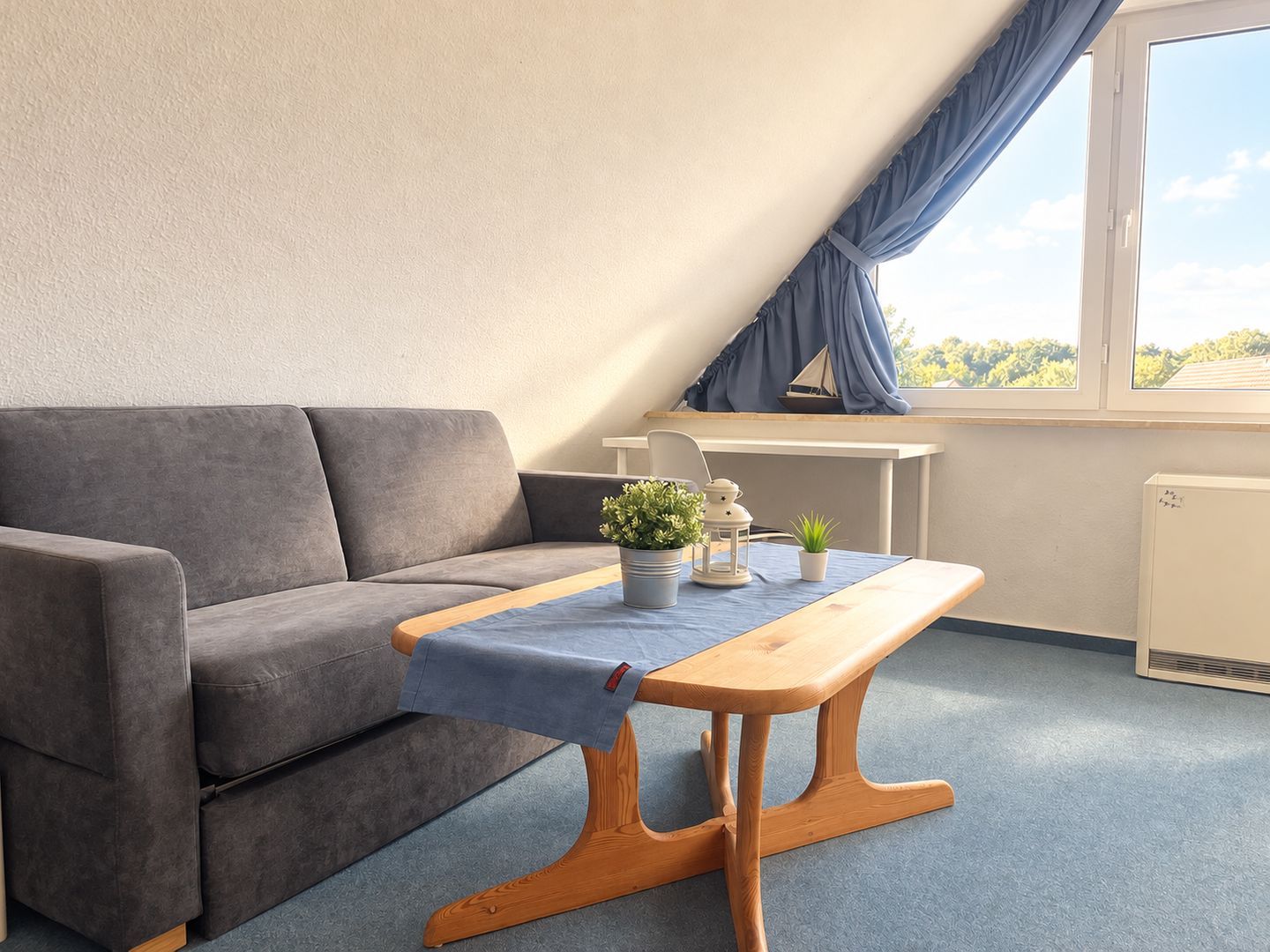 A modern room with a grey sofa, a wooden table, and a small potted plant.