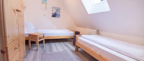 Una habitación pequeña y triangular con dos camas de madera, un armario de madera y un tragaluz.