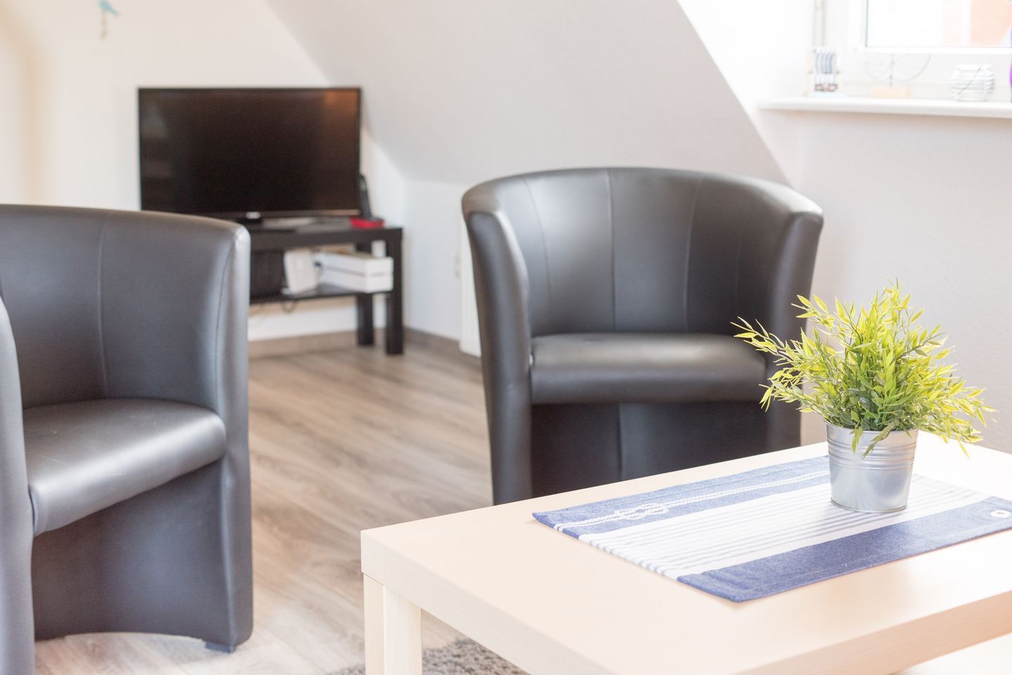 Ein modernes Wohnzimmer mit zwei schwarzen Ledersesseln, einem Holztisch und einem kleinen Topfpflanzen.