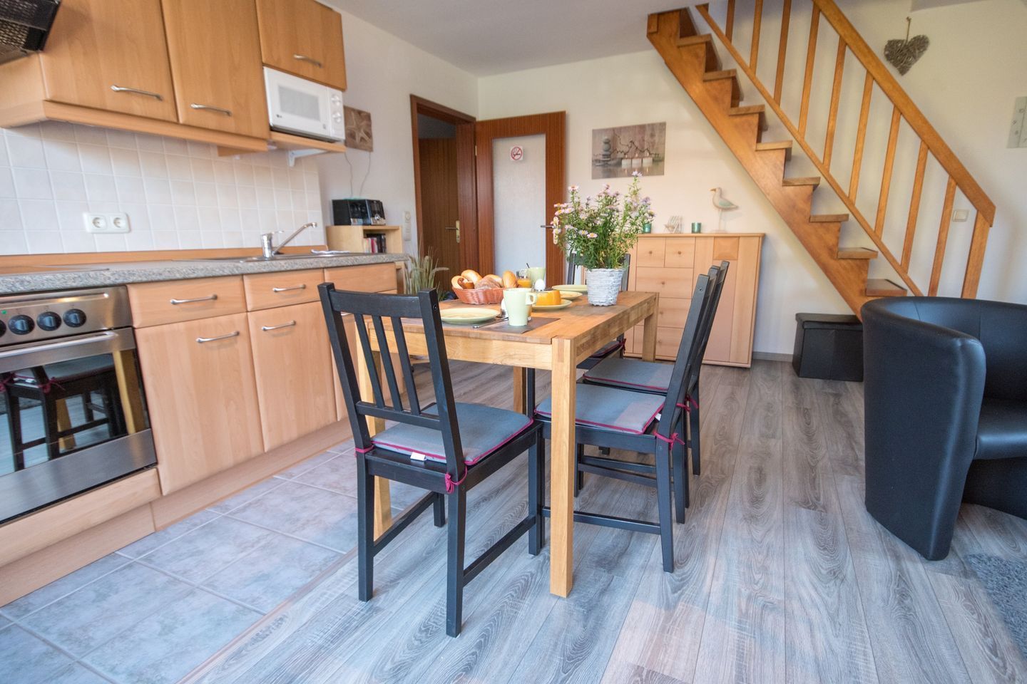 Eine kleine Küche mit Holzschränken, einem eingebauten Ofen und einem Esstisch mit Stühlen.