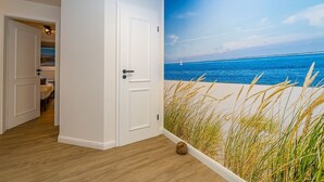 A room with a beach mural, wooden flooring, and a white door. - Wanlik Hüs I - 3-room vacation apartment, for max. 3 persons with terrace. (Sylt)