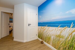 A room with a beach mural, wooden flooring, and a white door. - Wanlik Hüs I - 3-room vacation apartment, for max. 3 persons with terrace. (Sylt)