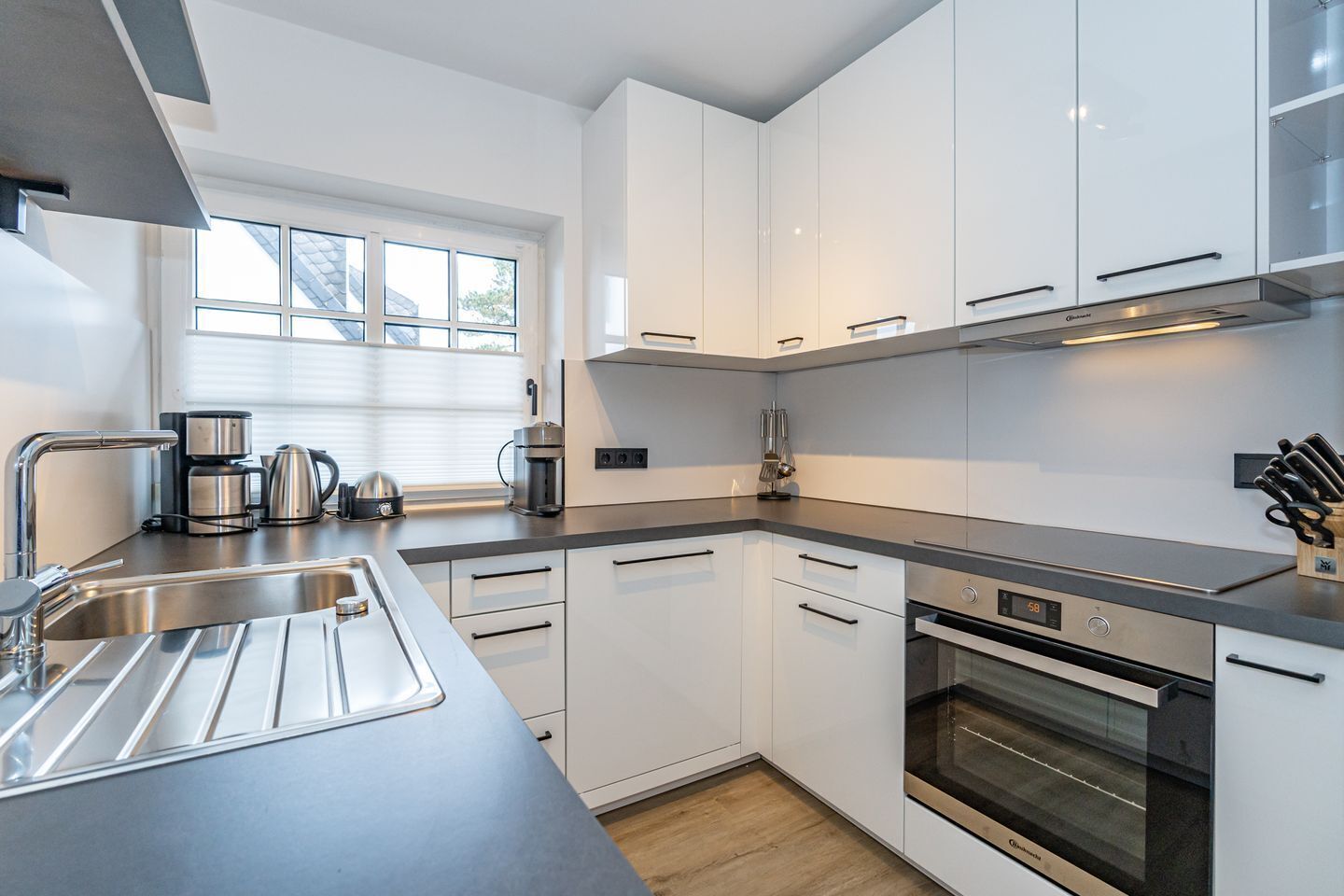 Una cocina moderna con armarios blancos, electrodomésticos de acero inoxidable y un amplio ventanal que proporciona luz natural.