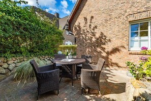 Une terrasse extérieure avec des meubles en osier, un mur en pierre et un bâtiment en briques en arrière-plan.