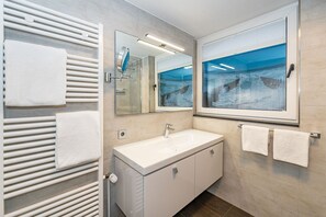 A modern bathroom with a white sink, a large mirror, and a window with a view of the ocean. - Wanlik Hüs I - 3-room vacation apartment, for max. 3 persons with terrace. (Sylt)