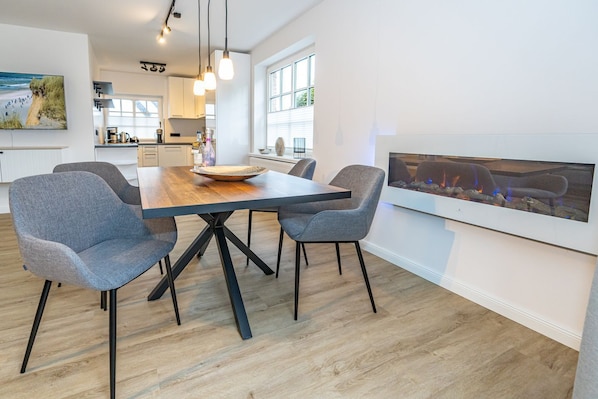 Un espace repas moderne avec une table en bois, quatre chaises grises à revêtement rembourré et des luminaires suspendus.