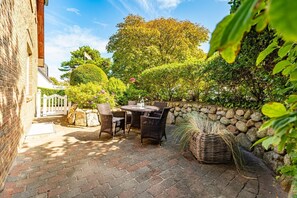 An outdoor patio with a stone wall, wicker furniture, and a neatly trimmed hedge. - Wanlik Hüs I - 3-room vacation apartment, for max. 3 persons with terrace. (Sylt)