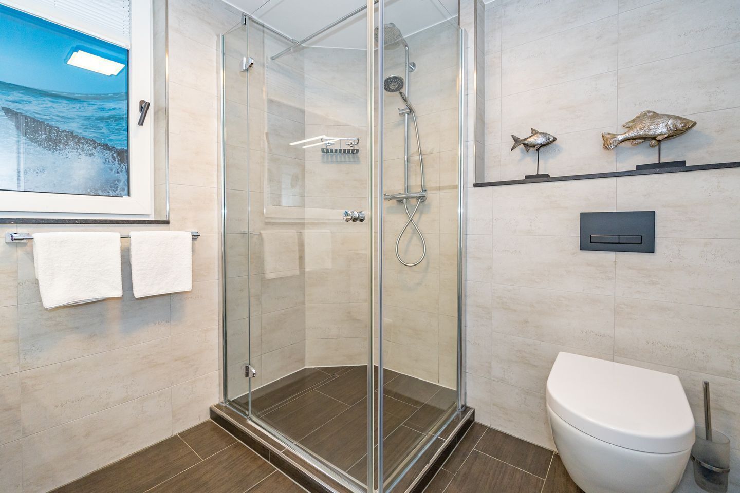 Et moderne badeværelse med en glasafskærmet brusekabine, toilet og en hylde med dekorative fisk.
