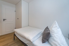 Une petite chambre avec un lit simple, un plancher en bois, des murs blancs et une porte blanche.