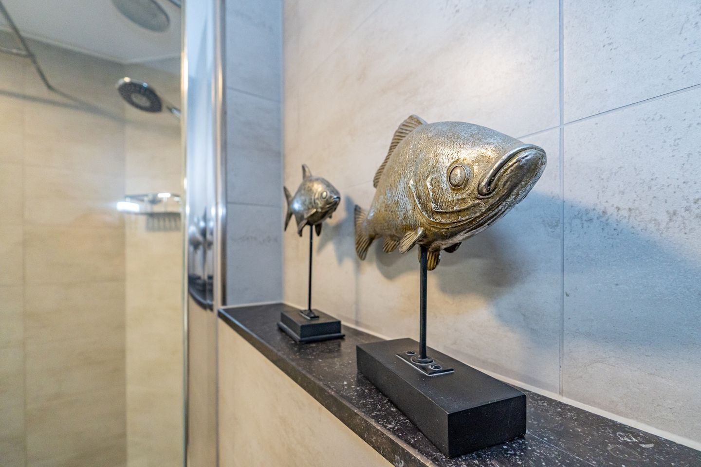 A bathroom with a marble wall and a shelf displaying two fish sculptures.