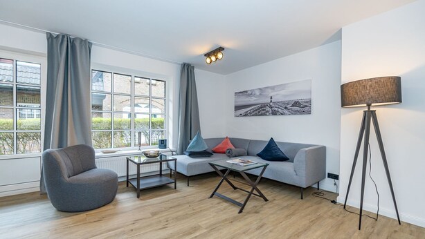 A modern living room with a grey sofa, a glass coffee table, a grey armchair, and a floor lamp. - Wanlik Hüs I - 3-room vacation apartment, for max. 3 persons with terrace. (Sylt)