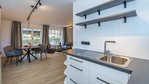 A modern kitchen with a built-in sink, white cabinetry, and a dining area with a table and chairs. - Wanlik Hüs I - 3-room vacation apartment, for max. 3 persons with terrace. (Sylt)