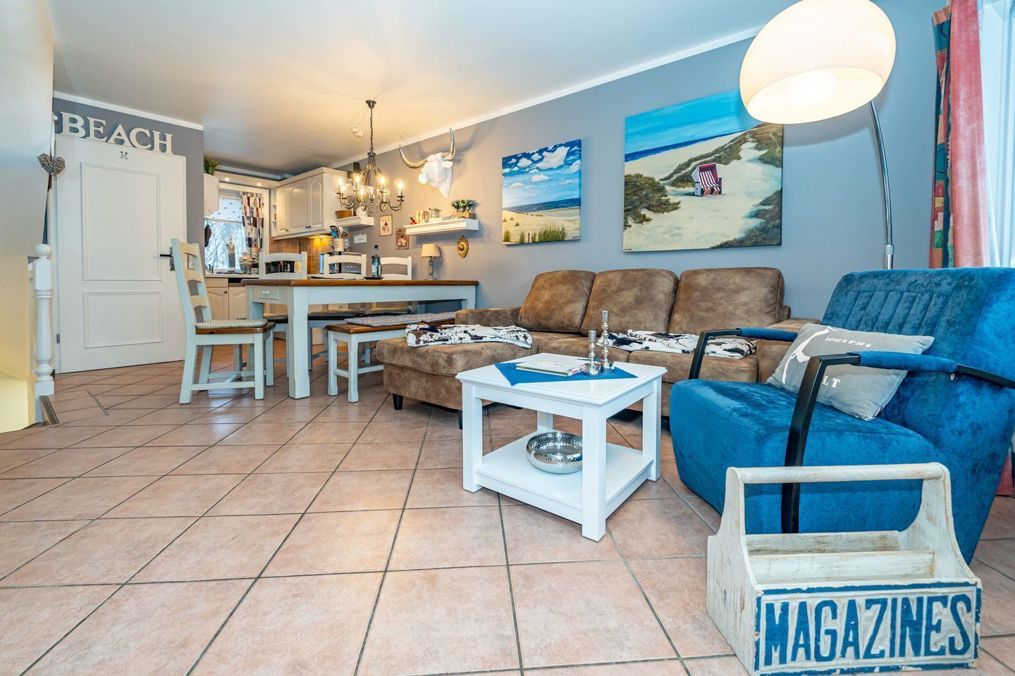 A living room with a blue sofa, a white coffee table, and a kitchen area with a dining table and chairs.