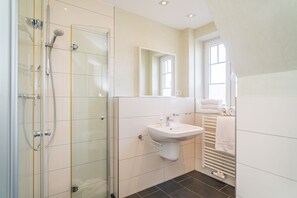 A modern bathroom with a glass-enclosed shower, a white sink, and a towel rack.