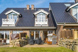 A two-story house with a sloped roof, dormer windows, and a stone wall in the front yard.