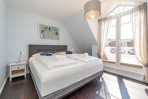 A bedroom with a bed, a nightstand, a painting, a window with curtains, and a view of the outside.