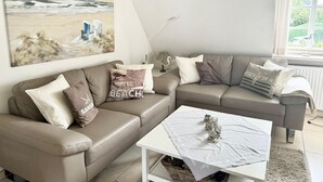 Un soggiorno moderno con un divano in pelle beige, un tavolino da caffè bianco e un quadro a tema spiaggia.