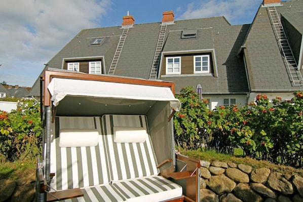 A convertible sofa bed with a canopy, set against a stone wall and surrounded by greenery. - Friesenglück - 3-room vacation apartment for up to 4 people with sunbathing area. (Sylt)