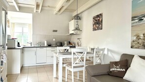 Una cucina moderna con mobili bianchi, un'area pranzo con sedie bianche e un divano grigio con un cuscino.