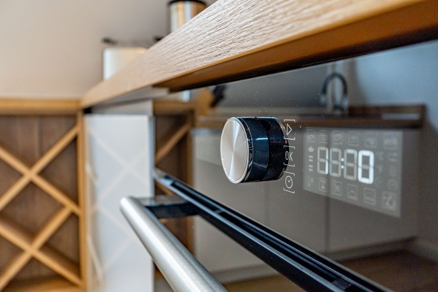 A kitchen with a digital clock displaying 8:00, a black knob, and a wooden countertop.
