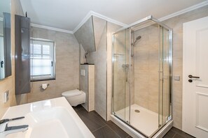 Een moderne badkamer met een douchekabinet van glas, een witte badkuip en een toilet.