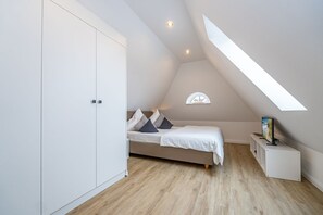 A bedroom with a sloped ceiling, a bed with pillows, a nightstand, a TV, and a wardrobe. - Wanlik Hüs II - Beautiful and quiet vacation apartment in Westerland for up to 3 people. (Sylt)