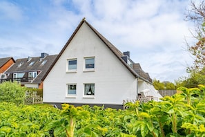 A white two-story house with a steeply pitched roof, multiple windows, and a visible chimney.