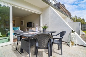 Un patio al aire libre con una mesa y sillas, un televisor al fondo y una pared exterior blanca.