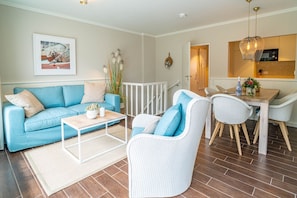 A modern living room with a blue sofa, white armchairs, a wooden coffee table, and a dining area with a white table and chairs.
