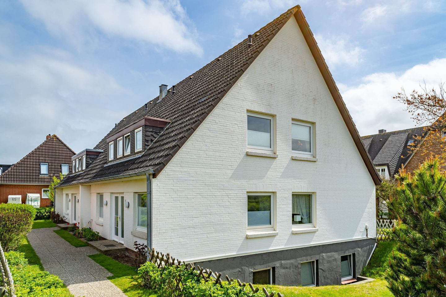 Een modern huis met twee verdiepingen, een schuin dak, witte buitenmuren en een klein voortuintje.