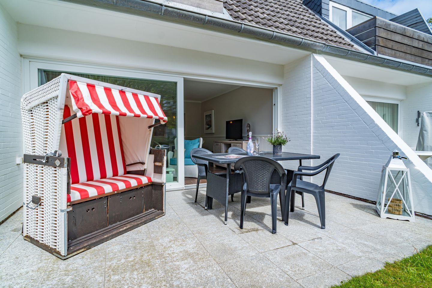 Eine Terrasse mit Korbmöbeln, einem Tisch mit Stühlen und einem weißen Laternenlicht.