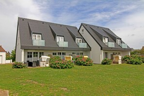Ein zweistöckiges Haus mit geneigtem Dach, zahlreichen Fenstern und einem gepflegten Garten mit Blumen und Rasen.