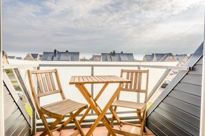Terraza en la azotea con dos sillas de madera y una mesa, con vistas a una hilera de casas.