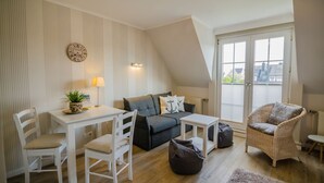 Une pièce confortable de style loft, comprenant une table à manger, des chaises blanches, un canapé gris, un fauteuil en osier et une petite table blanche.