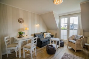 Un acogedor espacio tipo loft con mesa de comedor, sillas blancas, un sofá gris, un sillón de mimbre y una pequeña mesa blanca.