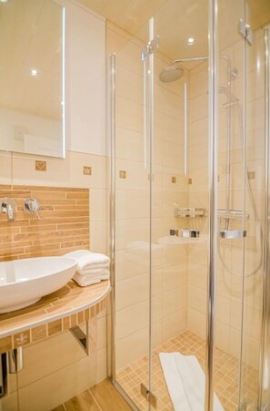 Un baño moderno con ducha acristalada, lavamanos blanco y salpicadero de azulejos.