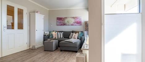 A spacious living area with a grey sofa, ottoman, and a large window providing natural light.