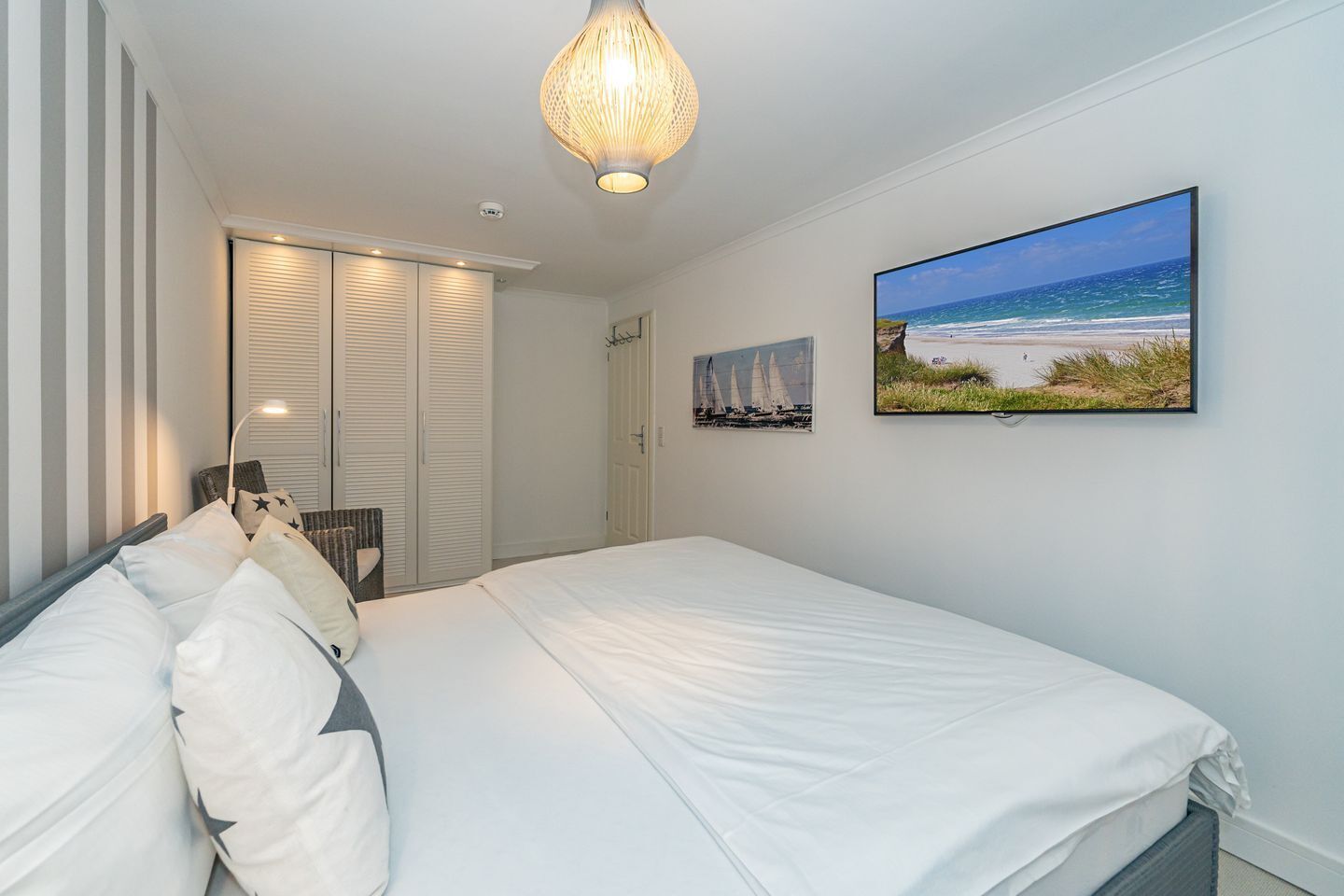 A bedroom with a bed, a hanging light fixture, a door, and a wall-mounted picture of a beach scene.