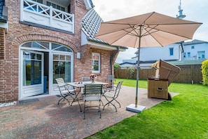 A patio with a table and chairs, a large umbrella, and a wooden cabinet.