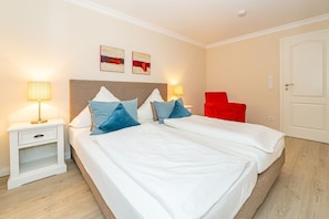 A hotel room with a double bed, two bedside tables with lamps, a red chair, and two wall-mounted artworks.