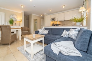 A modern living room with a grey sofa, a coffee table, and a dining area with wicker chairs.