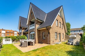 Ein zweistöckiges Haus mit Backsteinfassade, einem Ziegeldach und einer kleinen Terrasse mit Gartenmöbeln.